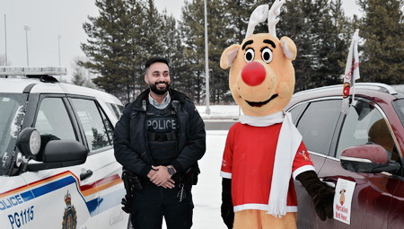 Photo de la mascotte de l'Opération Nez rouge et d'un agent de la GRC devant une voiture de police et un véhicule de bénévoles.