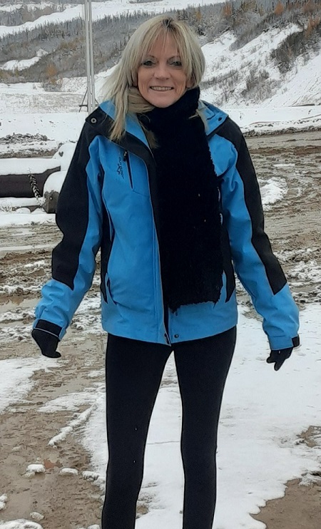 Femme avec les cheveux blonds qui porte un gilet bleu et un pantalon noir.