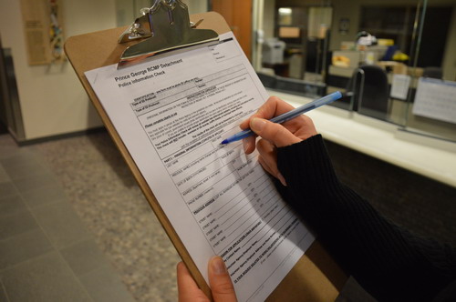 Image of the right hand of someone about to fill out a Police Information Check on a clipboard.